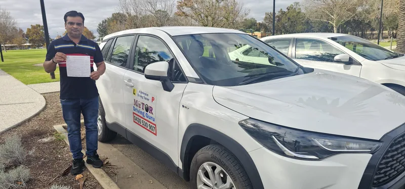 Learner in a striped polo holding a certificate beside the school SUV